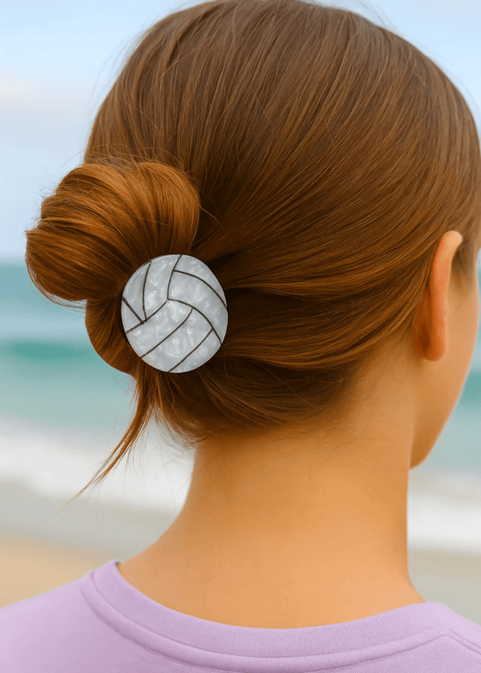 Person with a bun holding a volleyball on a beach
